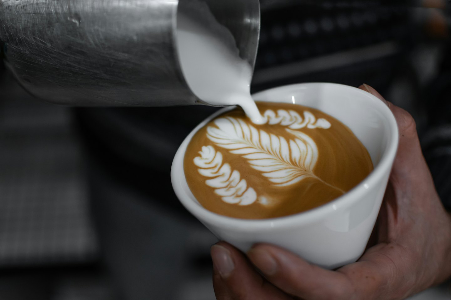 Barista vertiendo leche vaporizada para crear arte latte.