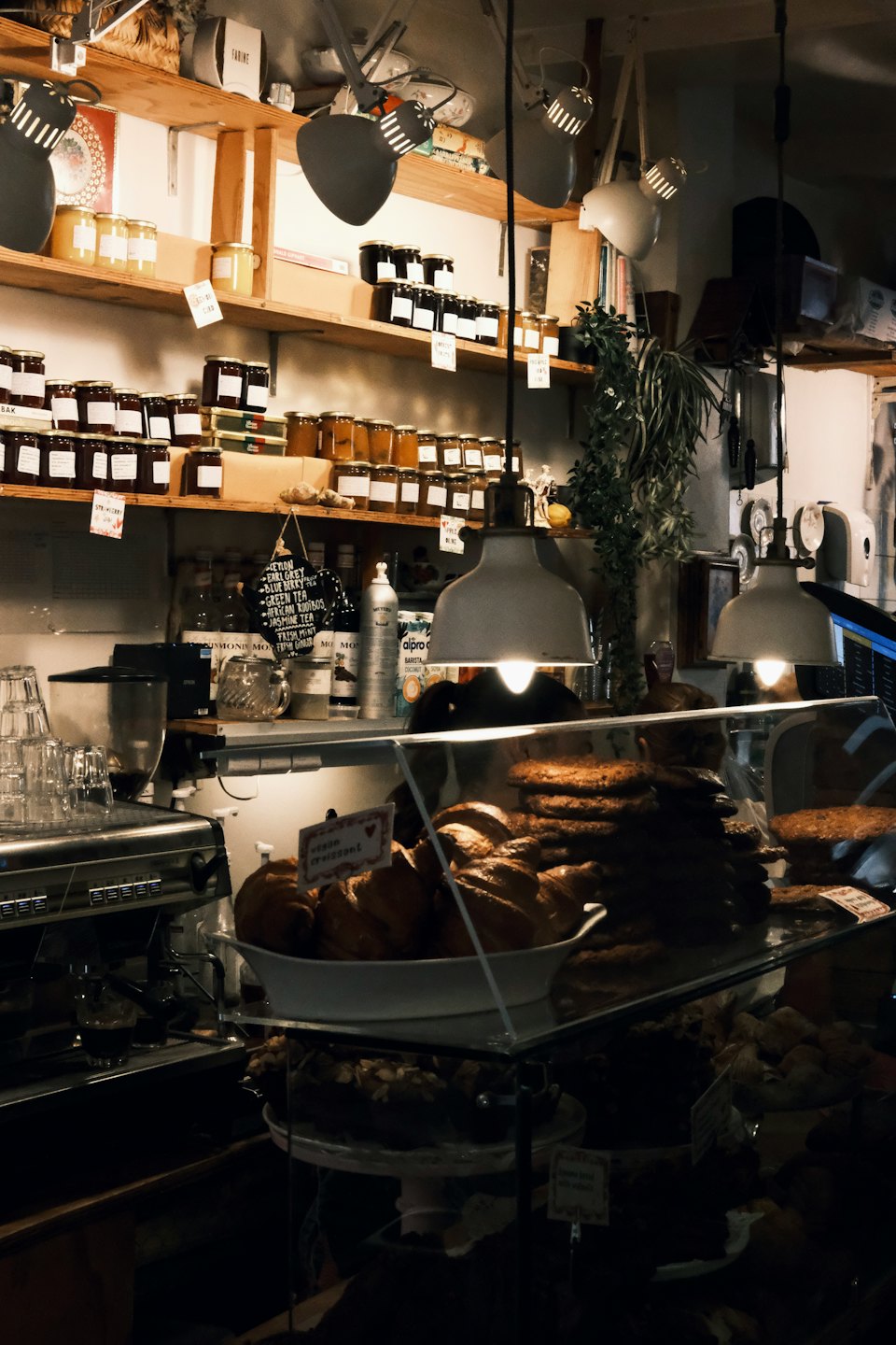 Mostrador de cafetería con pasteles, frascos de mermelada y máquina de espresso.